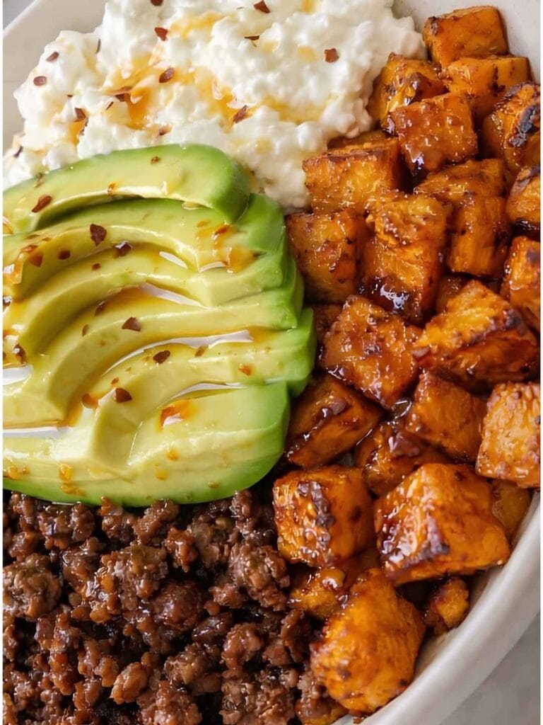 Savory, spiced ground beef sits next to perfectly caramelized roasted sweet potato cubes, buttery avocado slices, and a scoop of creamy cottage cheese.