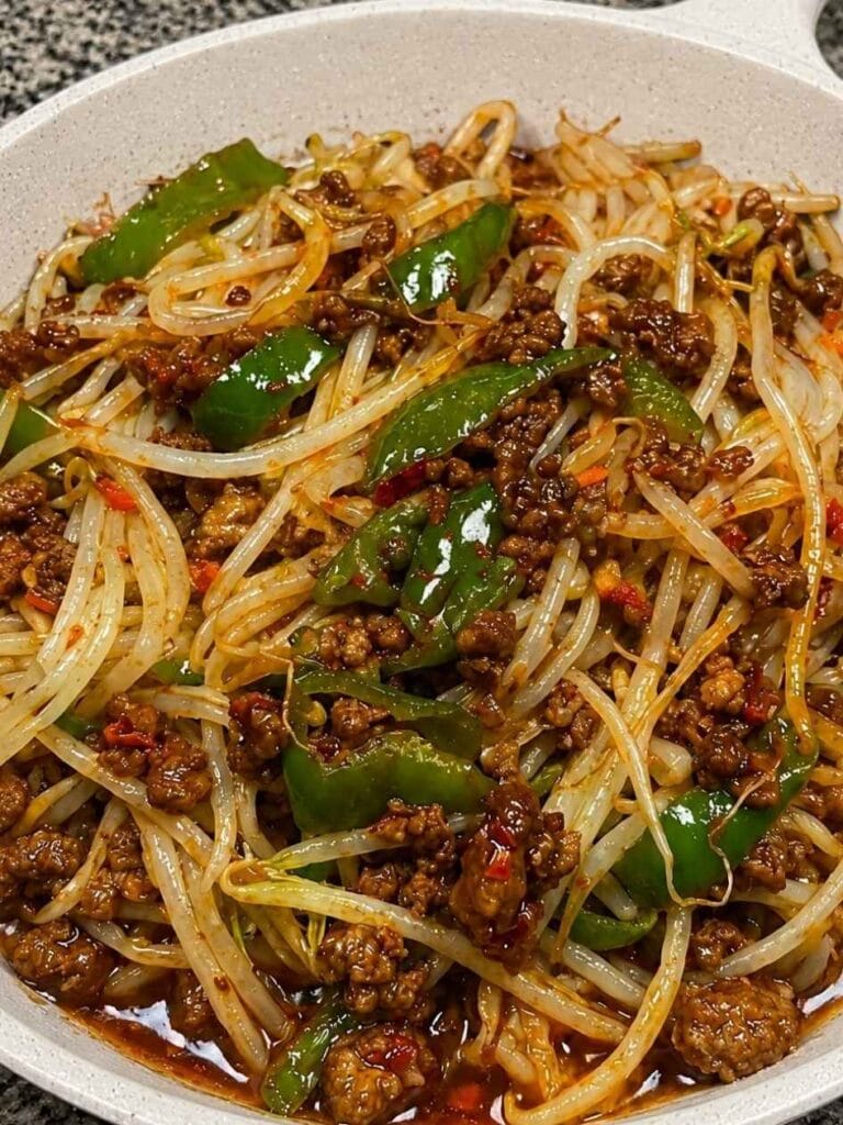 Crumbled ground beef, crisp mung bean sprouts, and sliced green chili peppers sit tangled together in a glossy, deep red-brown sauce, with visible flecks of crushed red pepper throughout.